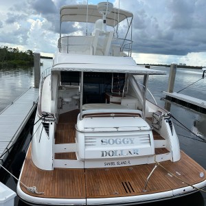 Rear view of a yacht named 'Soggy Dollar' docked at a marina on a cloudy day.
