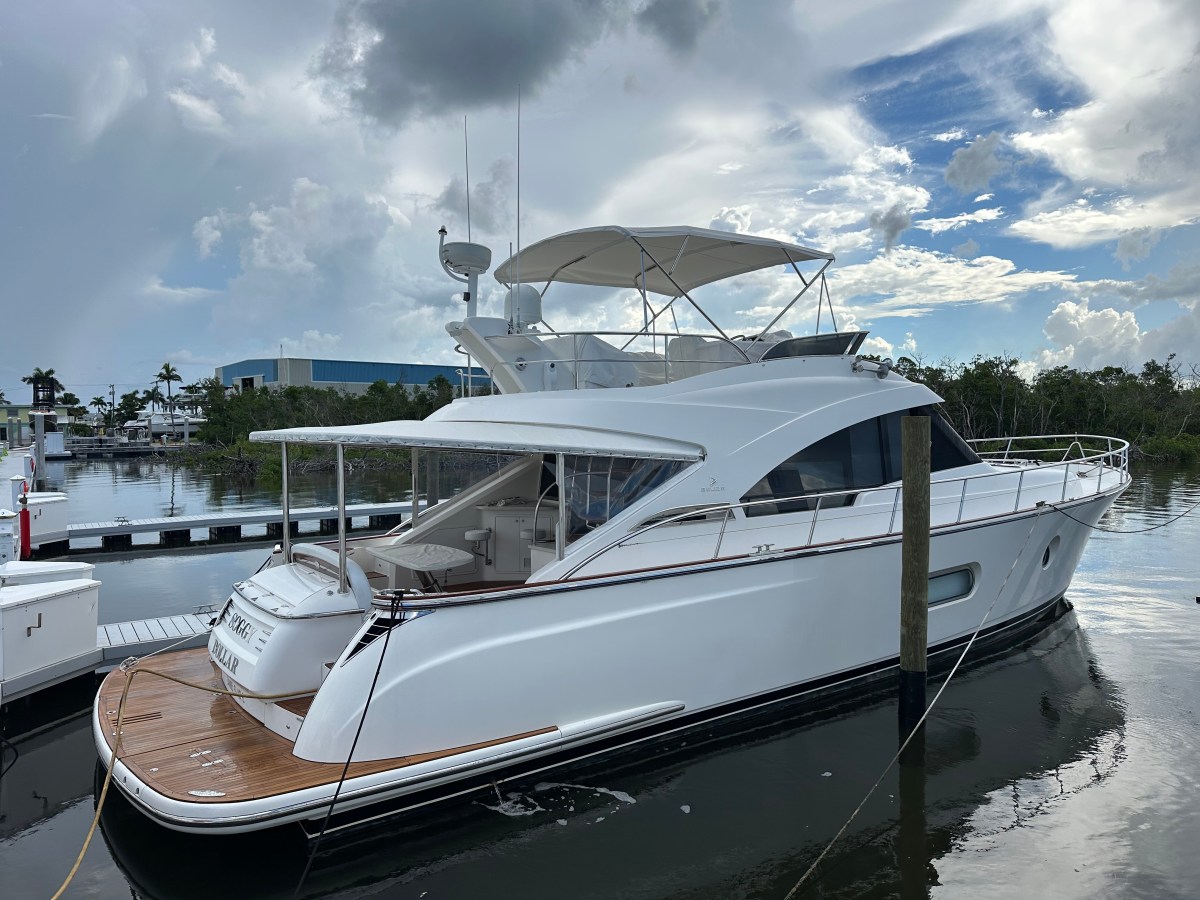 A white luxury yacht docked at a marina under a cloudy sky.