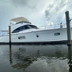 White yacht docked on calm water, cloudy sky in background.