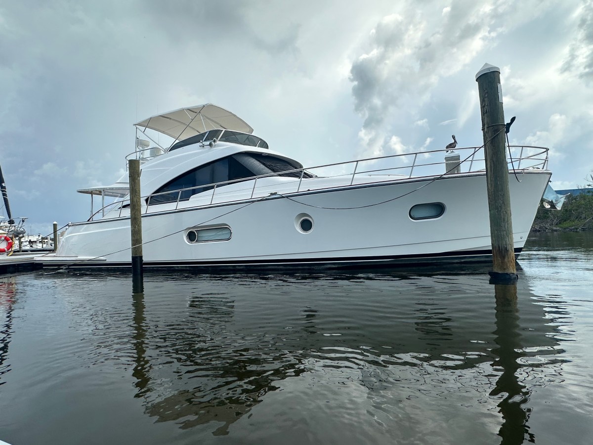 White yacht docked on calm water, cloudy sky in background.