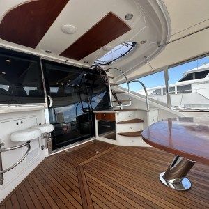 Luxury yacht deck with wooden floor, table, stairs, and glass doors.