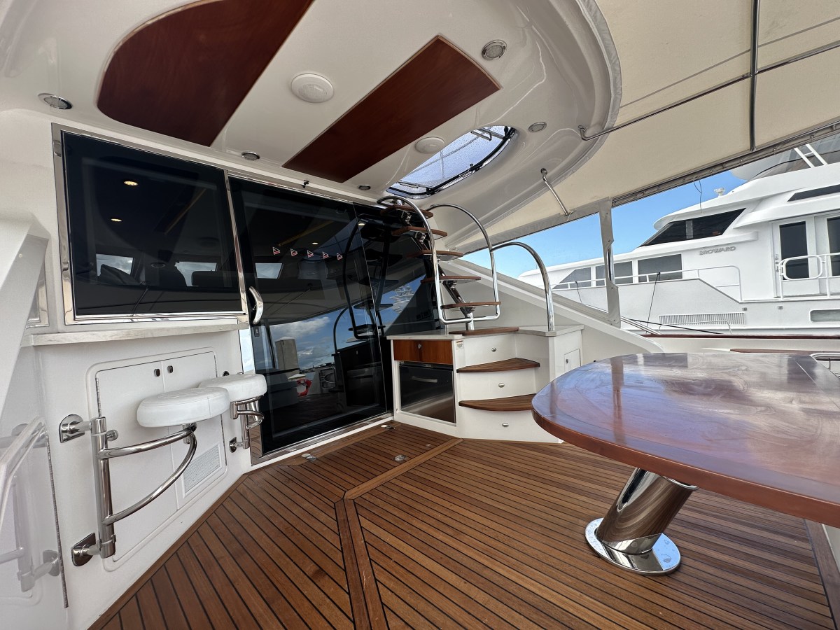 Luxury yacht deck with wooden floor, table, stairs, and glass doors.
