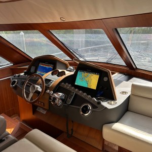 Boat helm with steering wheel, navigation screens, and leather seats in sunlight.