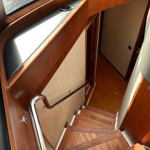 Wooden staircase in a boat with metal handrail and sunlight shining through a window.
