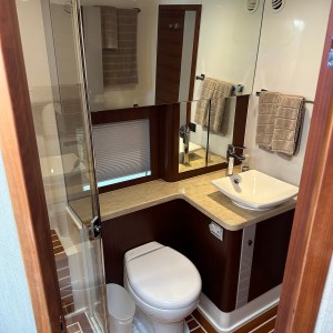 Compact bathroom with wood accents, toilet, sink, shower, and towels on racks.