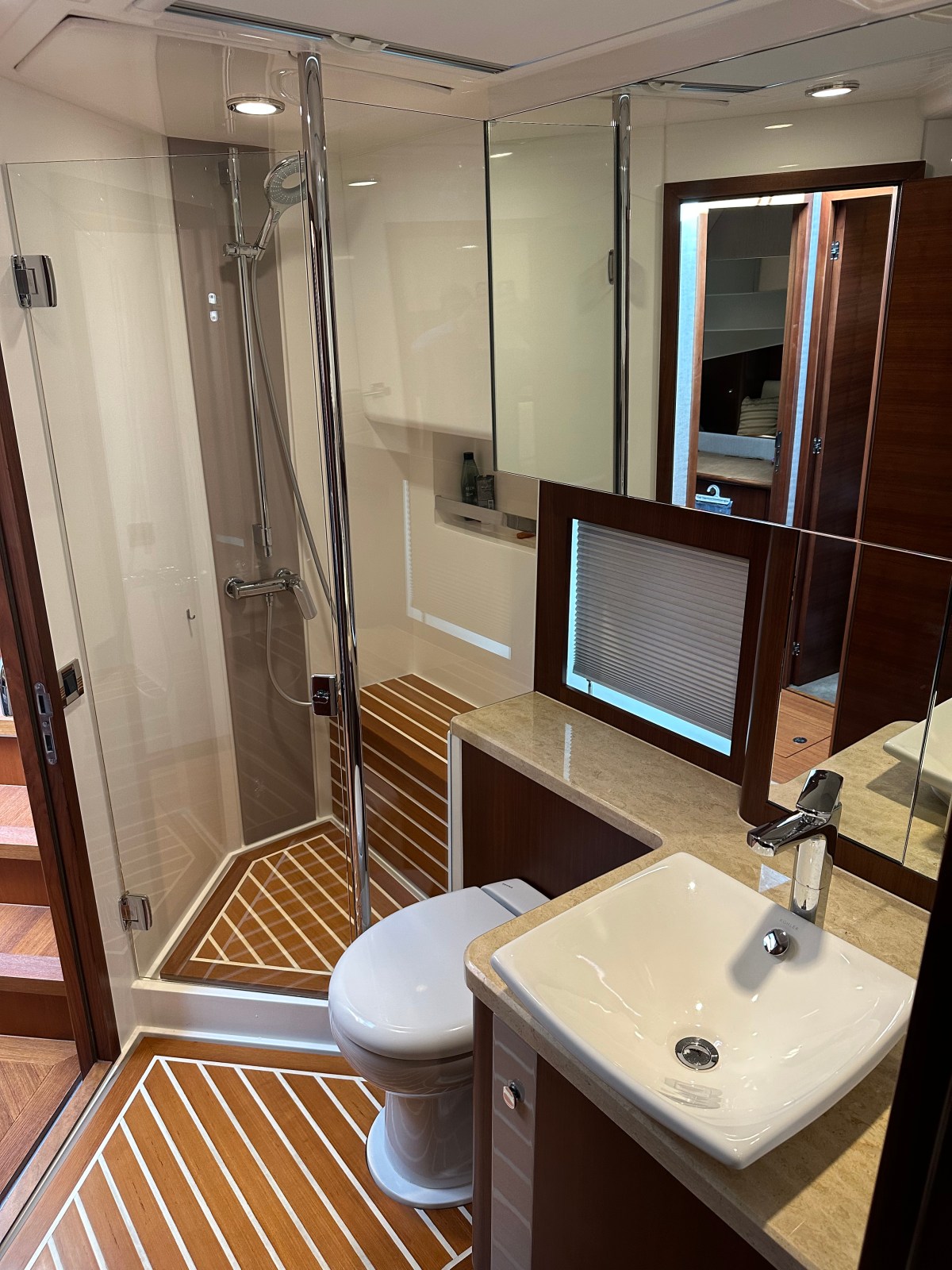 Modern bathroom with glass shower, white sink, toilet, and wood accents on floor and platform.