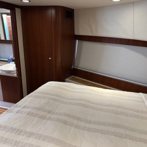 Cozy bedroom with striped bedding, a window with a blind, and a view into a bathroom.