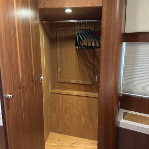 Open wooden closet with a metal rod and several black hangers inside.