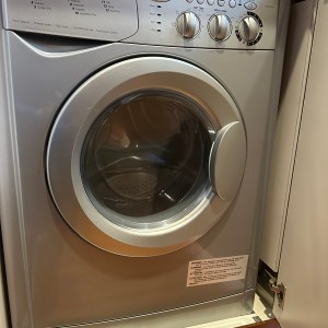 Silver front-loading washing machine inside a cabinet with control knobs.