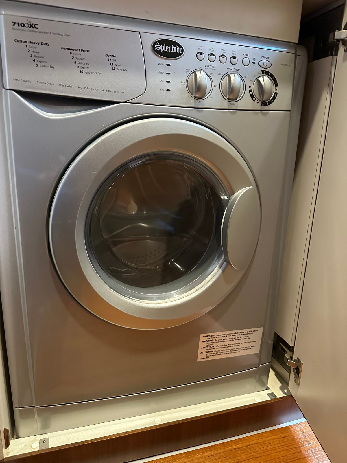 Silver front-loading washing machine inside a cabinet with control knobs.
