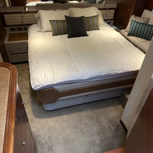 Cozy bedroom with striped pillows, white bedding, beige carpet, wooden accents, and ambient lighting.