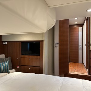 Modern yacht bedroom with TV, bed, cushions, and open door to hallway.