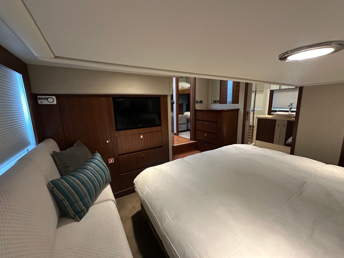 Cozy bedroom with bed, sofa, TV, and wooden cabinets on luxury yacht.