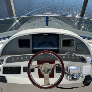 Yacht helm with steering wheel and control panels overlooking calm water.