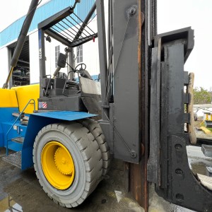 Close-up of a large forklift with yellow wheels and a load handling attachment, outside a blue building.