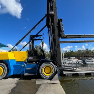 Large forklift on a dock next to the water under a blue sky with clouds.