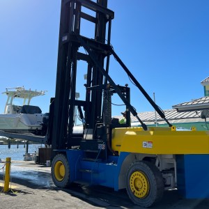 Forklift lifting a boat near a waterfront building on a sunny day.