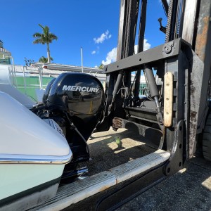 Forklift lifting a boat, with a Mercury motor exposed, against a clear blue sky.